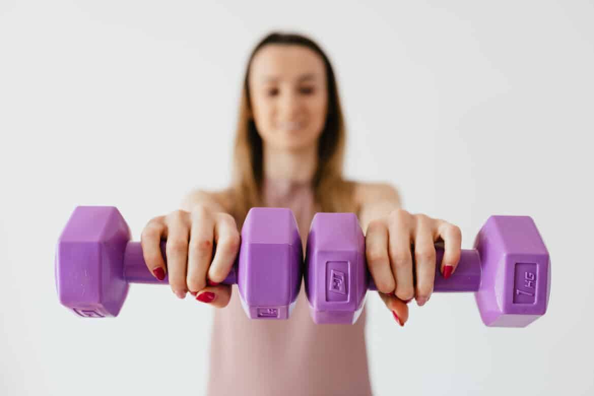 Purple dumbbells in hands of positive sportswoman